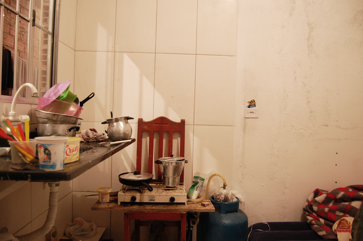 Cozinha de uma das casas: o fogão portátil comprado pelos trabalhadores ficava em cima de uma cadeira, ligado ao botijão de gás no pé do colchão de ar onde um deles dormia (Foto: Stefano Wrobleski)
