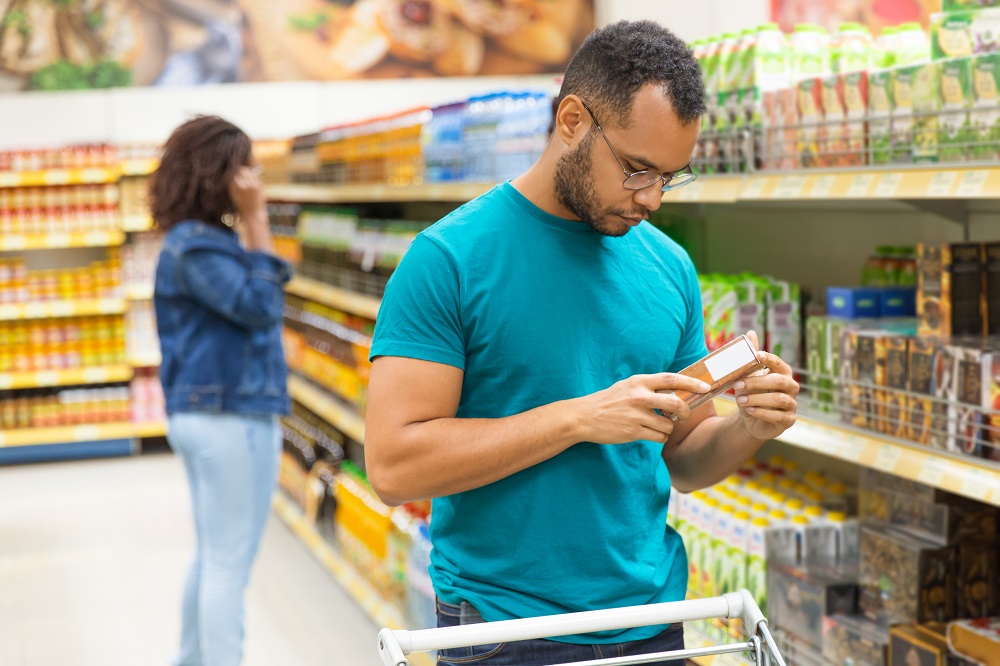 Homem lê rótulo de alimento ultraprocessado no supermercado