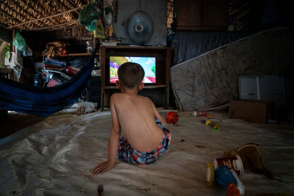 Menino assiste a desenhos animados no barraco de lona em que vive com a família no Acampamento Nova Aliança, em Itanhangá, no Mato Grosso. Desde 2014, cerca de 70 famílias sem terra vivem em um único lote a espera de uma decisão do Incra (Foto: Fernando Martinho/Repórter Brasil)