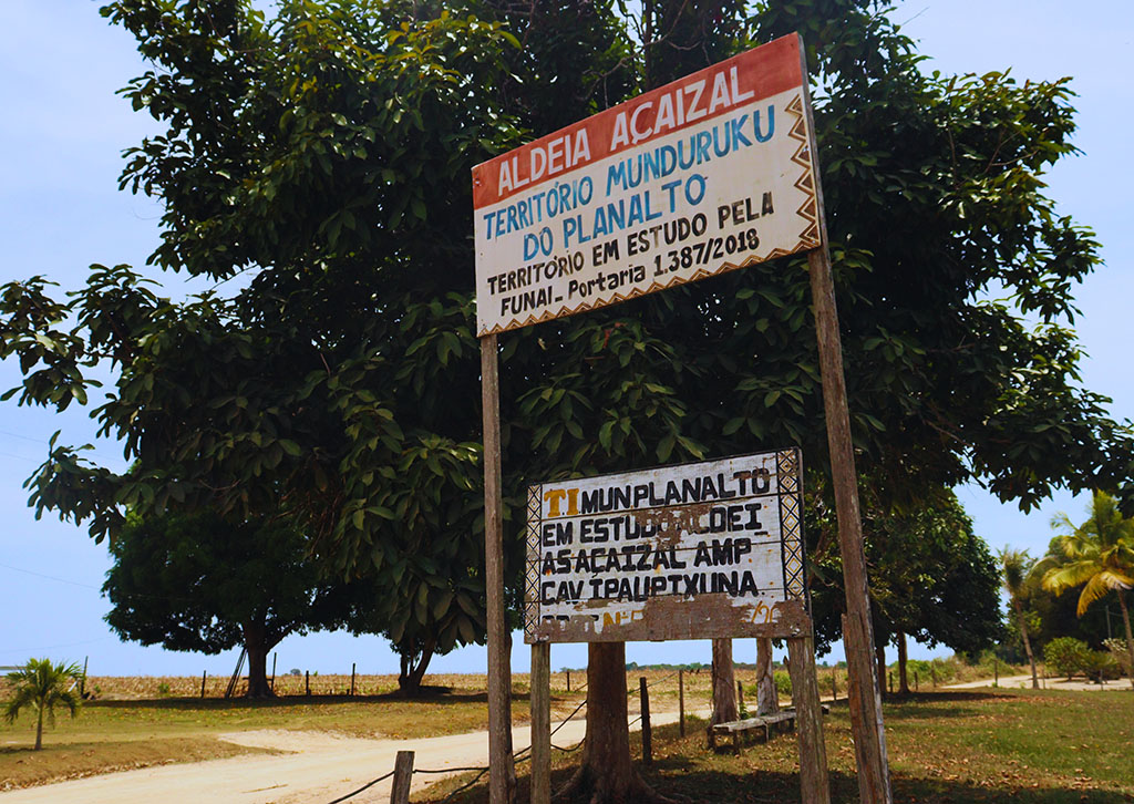 Placa na entrada da aldeia Açaizal, na TI Planalto Santareno, onde vivem famílias Munduruku e Apiaká. Ao fundo, campos de soja (Foto: José Marcos Tapajós/Tapajós de Fato)