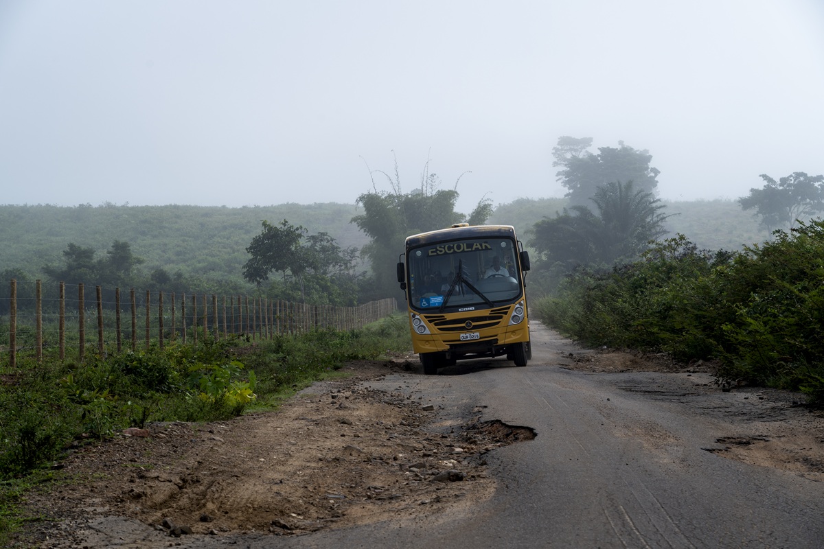 Ônibus escolar desvia de buracos na BA880. A estrada corta a plantação de macaúba da Acelen e conecta diversas comunidades quilombolas do Recôncavo Baiano (Foto: Fernando Martinho/Repórter Brasil/27 de abril de 2026)