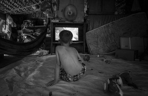 Itanhangá, Mato Grosso, Brasil 13-09-2023 Menino assistindo desenhos na TV no barraco de lona em que vive com a família no Acampamento Nova Aliança. Série de reportagens do projeto Pulitzer Center sobre violência no campo. Percorremos assentamentos e acampamentos em várias cidades do Mato Grosso e Pará, mostrando como a política do governo do ex–presidente Jair Bolsonaro amplificou a violência na Amazônia. ©Foto: Fernando Martinho